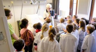 Een vrijwilligster legt uit aan de schoolkinderen welke onderzoeken er plaatsvinden bij een opname.