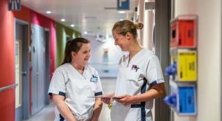 Twee verpleegkundigen overleggen in ziekenhuisgang